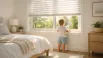 Child looking outside through a transparent window with summer blinds in a Canadian bedroom, wearing light summer clothes