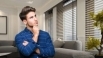 A man standing in a modern living room, looking thoughtful about the cost of blinds in Canada