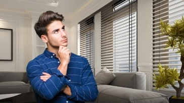 A man standing in a modern living room, looking thoughtful about the cost of blinds in Canada