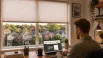 A homeowner researching a custom blinds company in Aurora, Ontario, on a laptop, with a residential view through large windows fitted with stylish blinds