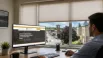 Business owner researching a custom blinds company in Newmarket, Ontario, on a computer, with a city view and window blinds visible through large office windows