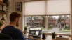 A homeowner researching a custom blinds company in Orillia, Ontario, on a laptop, with a residential view through large windows fitted with stylish blinds